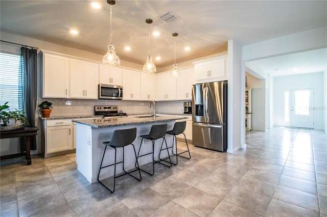kitchen with stone countertops, appliances with stainless steel finishes, a sink, a center island with sink, and a breakfast bar area