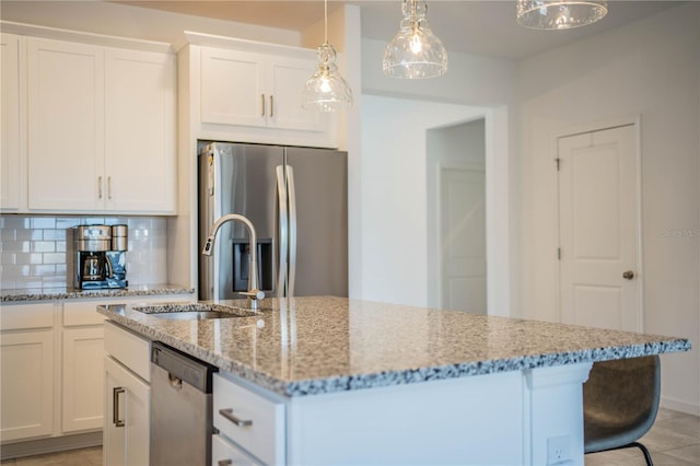 kitchen with white cabinets, a sink, a kitchen island with sink, stainless steel appliances, and light stone counters