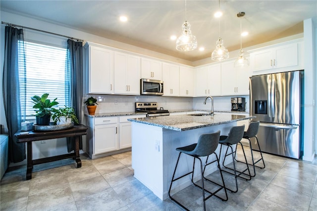 kitchen with an island with sink, white cabinetry, light stone countertops, appliances with stainless steel finishes, and a sink