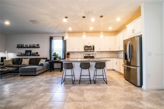 kitchen featuring light stone counters, hanging light fixtures, a kitchen island with sink, white cabinetry, and stainless steel appliances