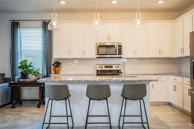 kitchen featuring white cabinetry, light stone countertops, a center island with sink, decorative backsplash, and appliances with stainless steel finishes