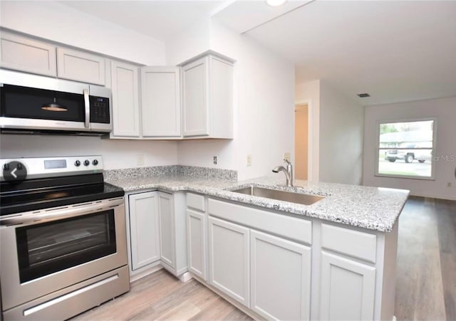 kitchen with light stone counters, light hardwood / wood-style floors, sink, kitchen peninsula, and stainless steel appliances