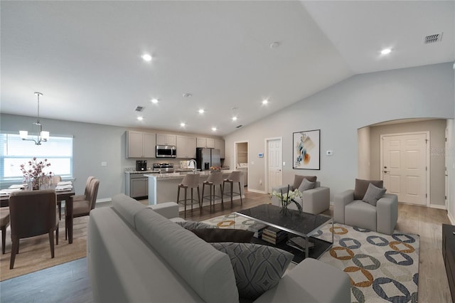 living room featuring an inviting chandelier, light hardwood / wood-style flooring, and vaulted ceiling