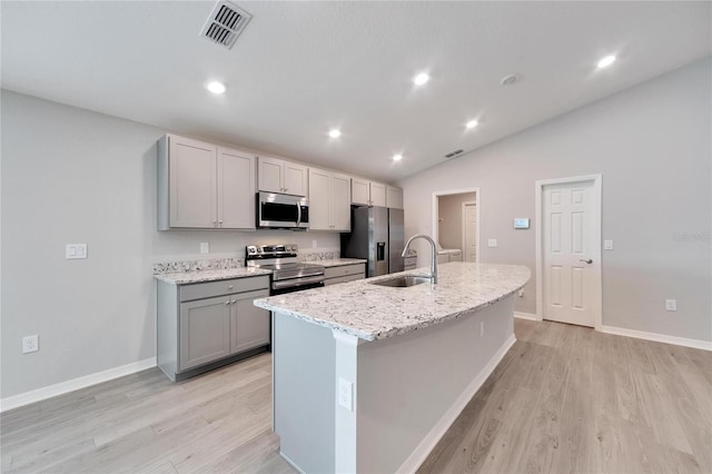 kitchen with gray cabinets, a kitchen island with sink, sink, vaulted ceiling, and appliances with stainless steel finishes