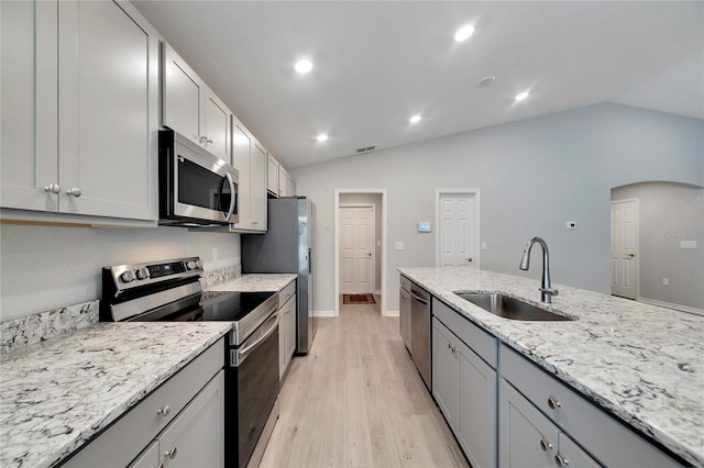 kitchen with appliances with stainless steel finishes, light wood-type flooring, vaulted ceiling, and sink