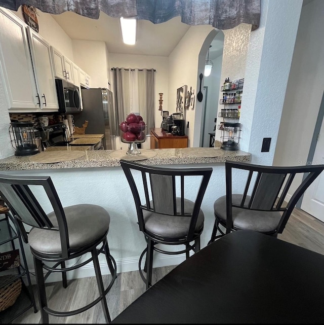 kitchen featuring appliances with stainless steel finishes, a breakfast bar, light hardwood / wood-style flooring, and kitchen peninsula