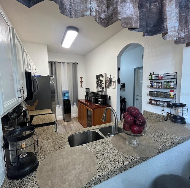 kitchen featuring light stone counters, white cabinetry, sink, kitchen peninsula, and light hardwood / wood-style flooring