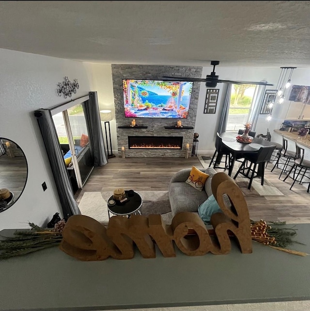 living room with a stone fireplace, hardwood / wood-style floors, and ceiling fan