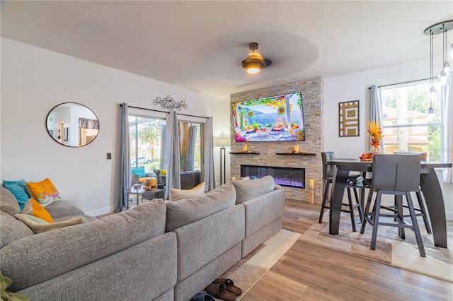 living room featuring a stone fireplace, wood-type flooring, and ceiling fan