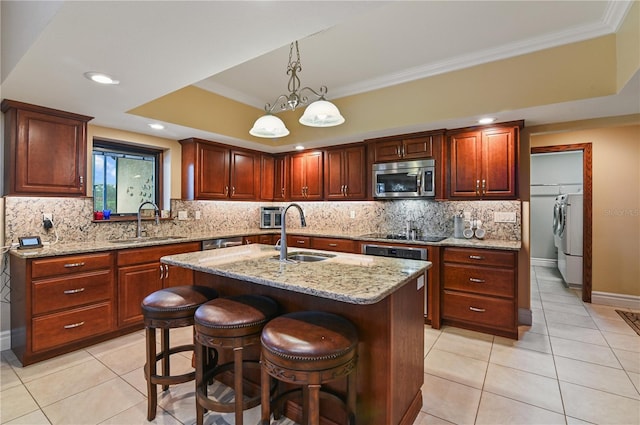 kitchen featuring light stone countertops, a tray ceiling, a center island with sink, and sink