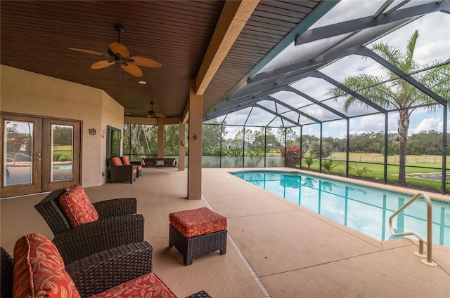 view of pool with glass enclosure, ceiling fan, a patio, and an outdoor living space