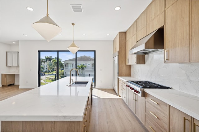 kitchen with sink, an island with sink, decorative light fixtures, appliances with stainless steel finishes, and light wood-type flooring