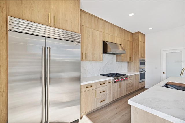 kitchen featuring wall chimney range hood, sink, light brown cabinetry, appliances with stainless steel finishes, and light hardwood / wood-style floors