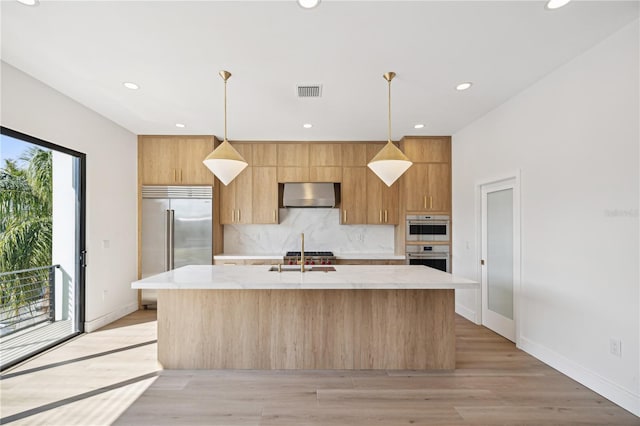 kitchen with a center island with sink, light wood-type flooring, decorative light fixtures, and ventilation hood