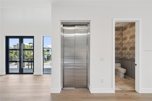 interior space with wood finished floors, toilet, elevator, baseboards, and french doors