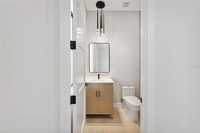 half bathroom featuring visible vents, baseboards, toilet, wood finished floors, and vanity