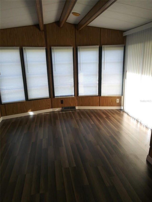 empty room with wood walls, wood finished floors, and beamed ceiling