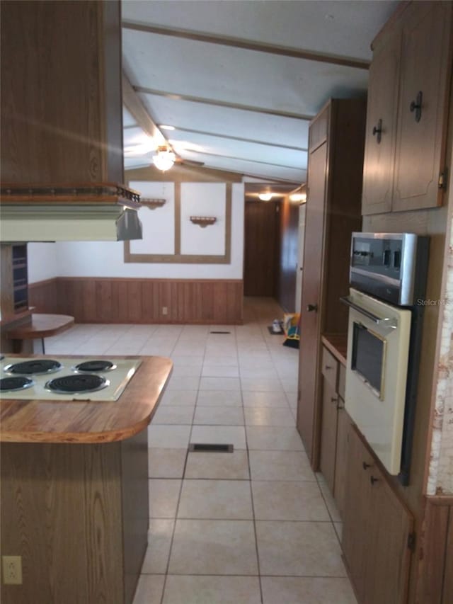 kitchen with wooden walls, vaulted ceiling, light tile patterned flooring, and white appliances
