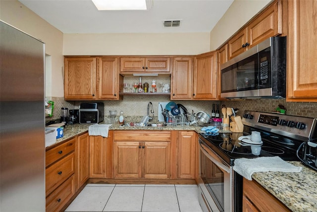 kitchen featuring sink, appliances with stainless steel finishes, tasteful backsplash, light stone countertops, and light tile patterned floors