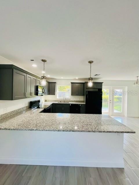 kitchen featuring light hardwood / wood-style floors, decorative light fixtures, light stone countertops, kitchen peninsula, and appliances with stainless steel finishes