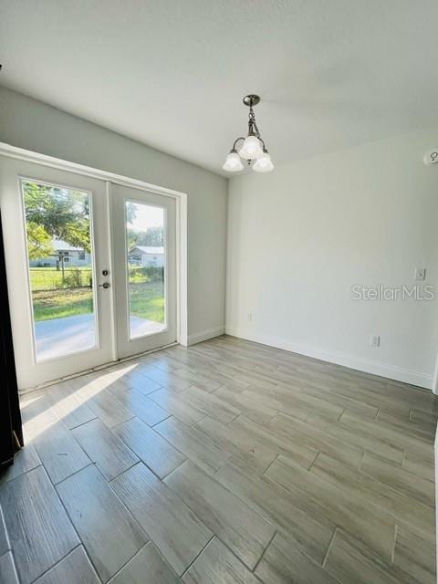 unfurnished room featuring french doors, an inviting chandelier, and light hardwood / wood-style floors