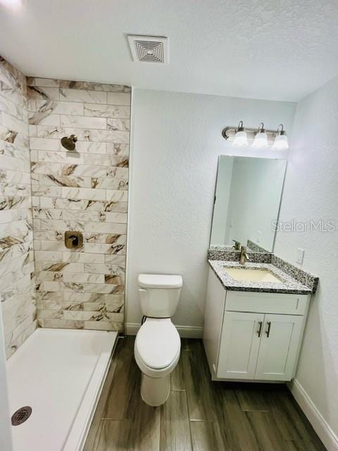 bathroom featuring toilet, hardwood / wood-style floors, tiled shower, vanity, and a textured ceiling