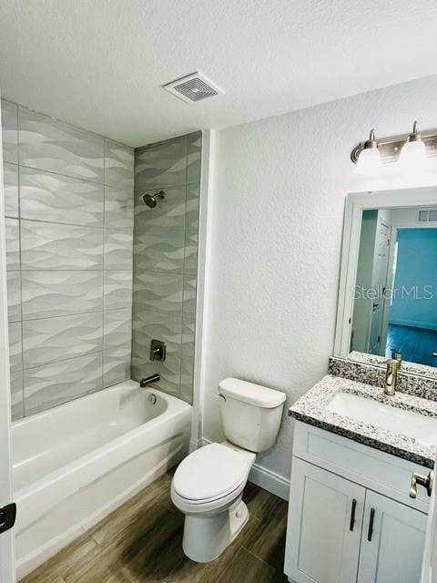 full bathroom featuring wood-type flooring, tiled shower / bath combo, vanity, and toilet