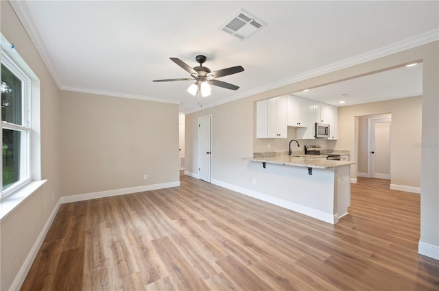 kitchen with white cabinets, kitchen peninsula, light hardwood / wood-style flooring, appliances with stainless steel finishes, and light stone countertops