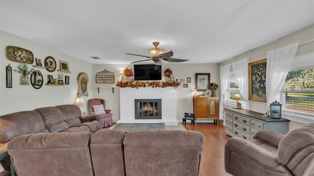 living room with a fireplace, light hardwood / wood-style flooring, a wealth of natural light, and ceiling fan