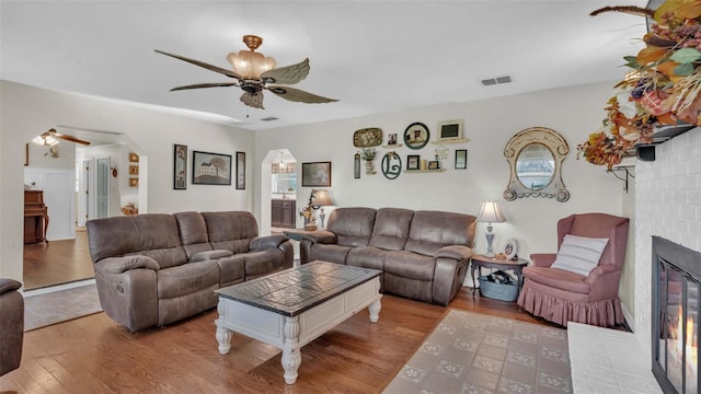 living room with ceiling fan, light hardwood / wood-style flooring, and a brick fireplace