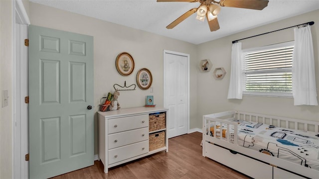 bedroom with ceiling fan, a closet, light hardwood / wood-style floors, and a crib