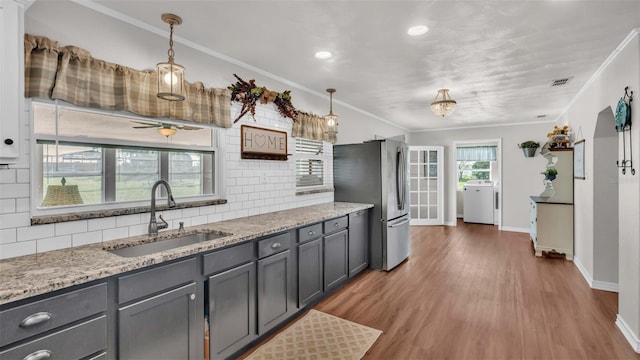 kitchen featuring decorative light fixtures, stainless steel fridge, ornamental molding, and sink