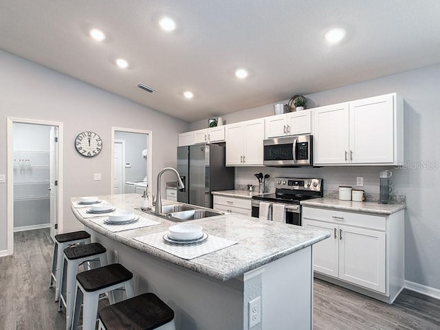 kitchen featuring white cabinets, a center island with sink, stainless steel appliances, and lofted ceiling