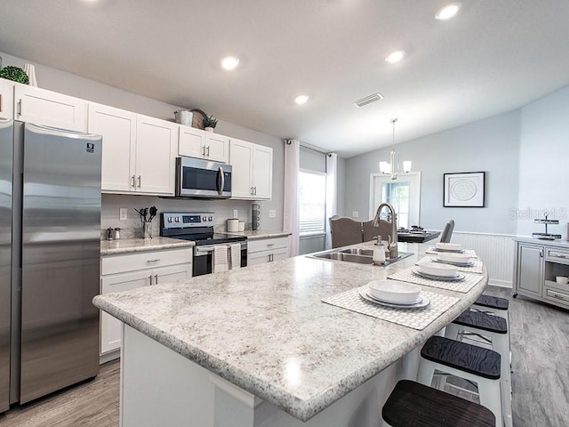 kitchen with vaulted ceiling, sink, hanging light fixtures, appliances with stainless steel finishes, and an island with sink