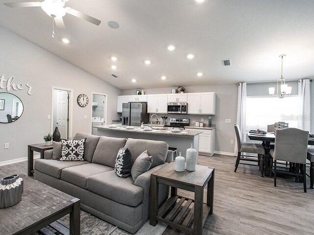 living room featuring vaulted ceiling, sink, ceiling fan with notable chandelier, and light hardwood / wood-style floors