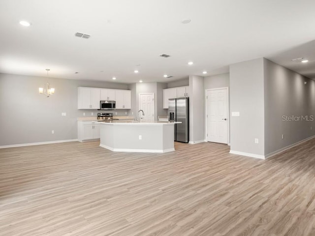 kitchen featuring stainless steel appliances, a center island with sink, light wood-type flooring, and white cabinetry