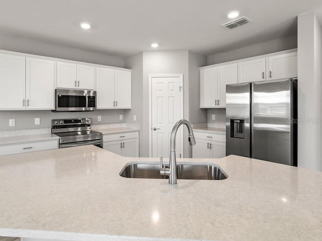 kitchen featuring appliances with stainless steel finishes, light stone countertops, sink, and white cabinets