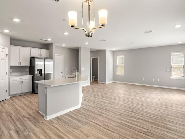 kitchen with light wood-type flooring, pendant lighting, sink, stainless steel refrigerator with ice dispenser, and white cabinetry