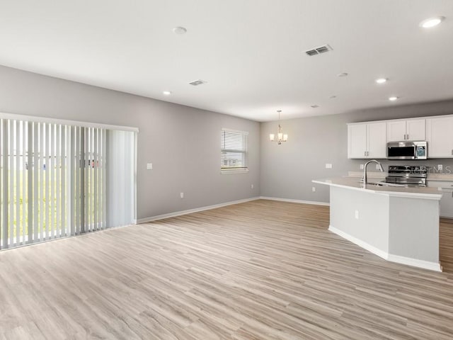 kitchen with white cabinets, sink, pendant lighting, light hardwood / wood-style flooring, and appliances with stainless steel finishes