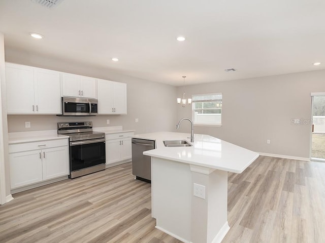 kitchen featuring a kitchen island with sink, sink, stainless steel appliances, and hanging light fixtures