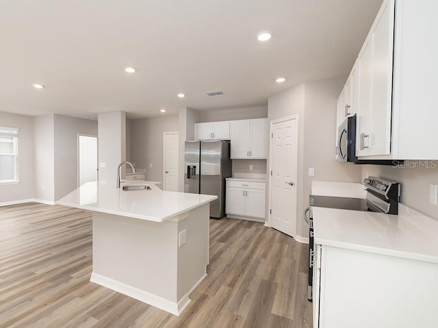 kitchen with appliances with stainless steel finishes, white cabinetry, an island with sink, sink, and light wood-type flooring