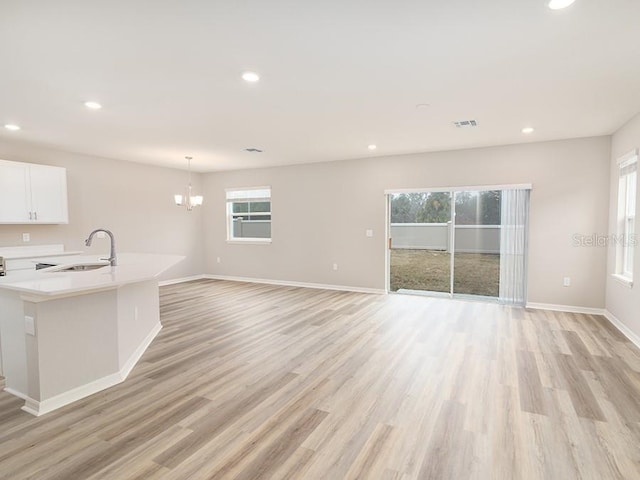 unfurnished living room with an inviting chandelier, sink, and light hardwood / wood-style floors