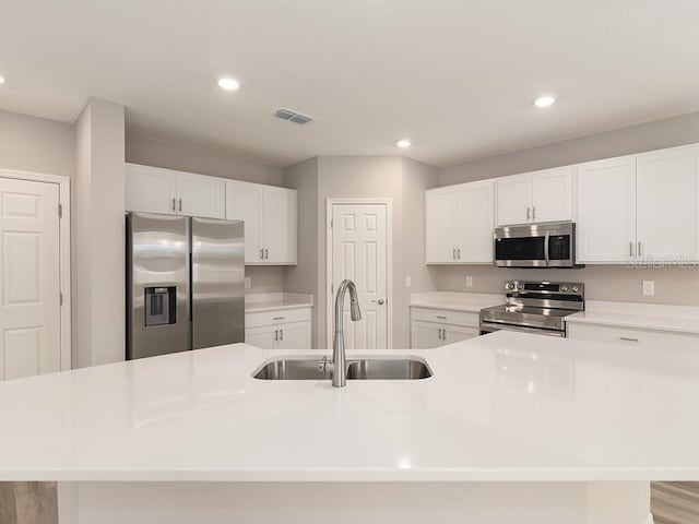 kitchen featuring sink, white cabinetry, a center island with sink, light hardwood / wood-style flooring, and appliances with stainless steel finishes