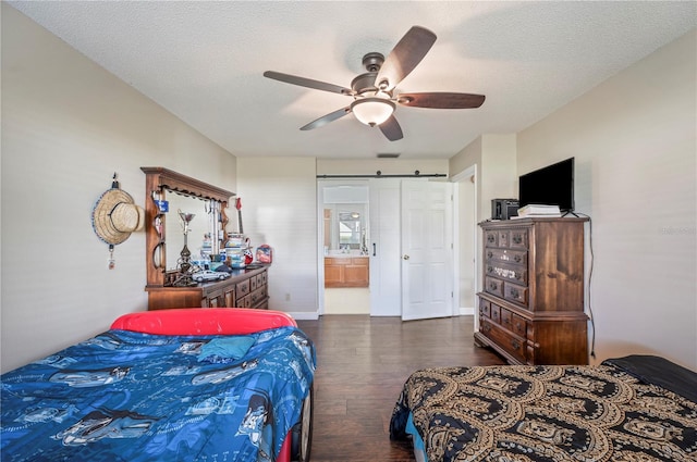 bedroom featuring ceiling fan, a textured ceiling, a barn door, dark hardwood / wood-style floors, and ensuite bath