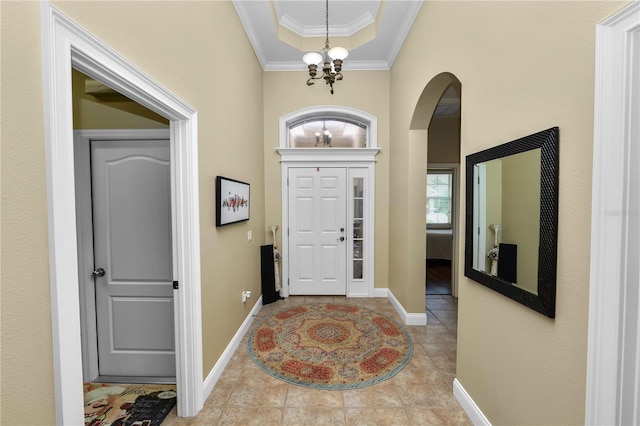 foyer entrance featuring tile patterned flooring, ornamental molding, arched walkways, baseboards, and a notable chandelier