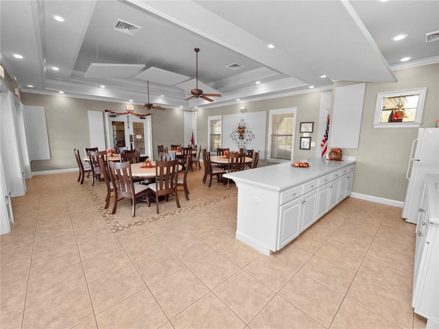 kitchen featuring kitchen peninsula, ceiling fan, white cabinetry, a tray ceiling, and crown molding