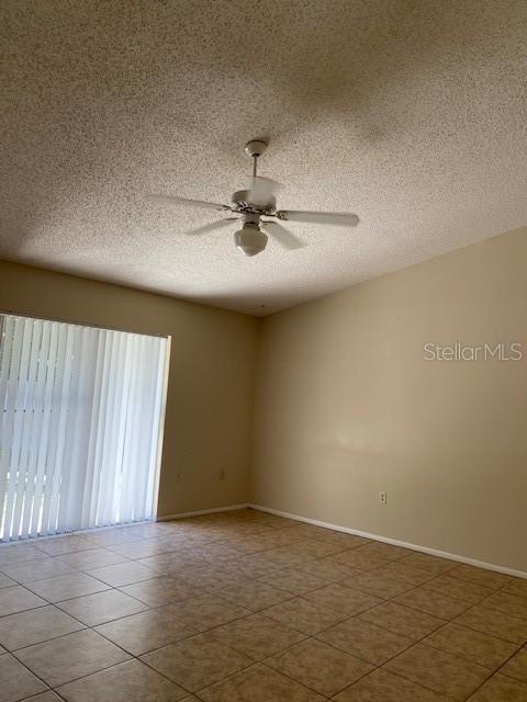 empty room featuring a textured ceiling, tile patterned floors, and ceiling fan