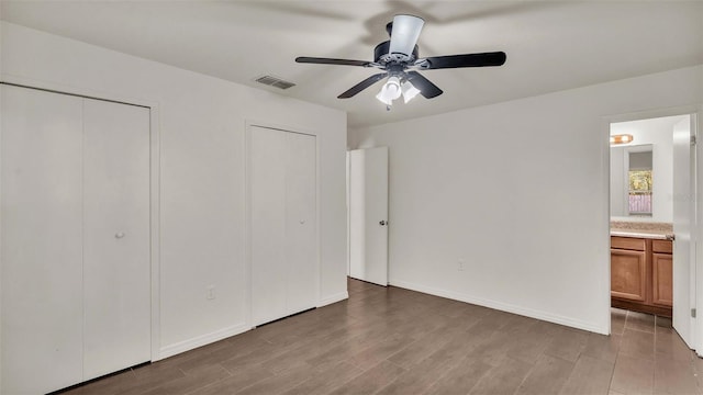 unfurnished bedroom with baseboards, visible vents, ensuite bathroom, light wood-style floors, and multiple closets