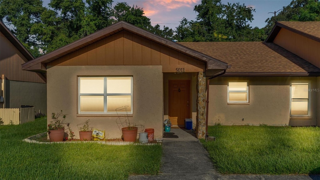 view of front of home featuring a front yard, roof with shingles, and stucco siding