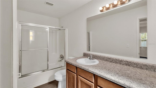 full bath with toilet, shower / bath combination with glass door, wood finished floors, visible vents, and vanity